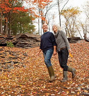 An older couple hikes through forest on an autumn day.