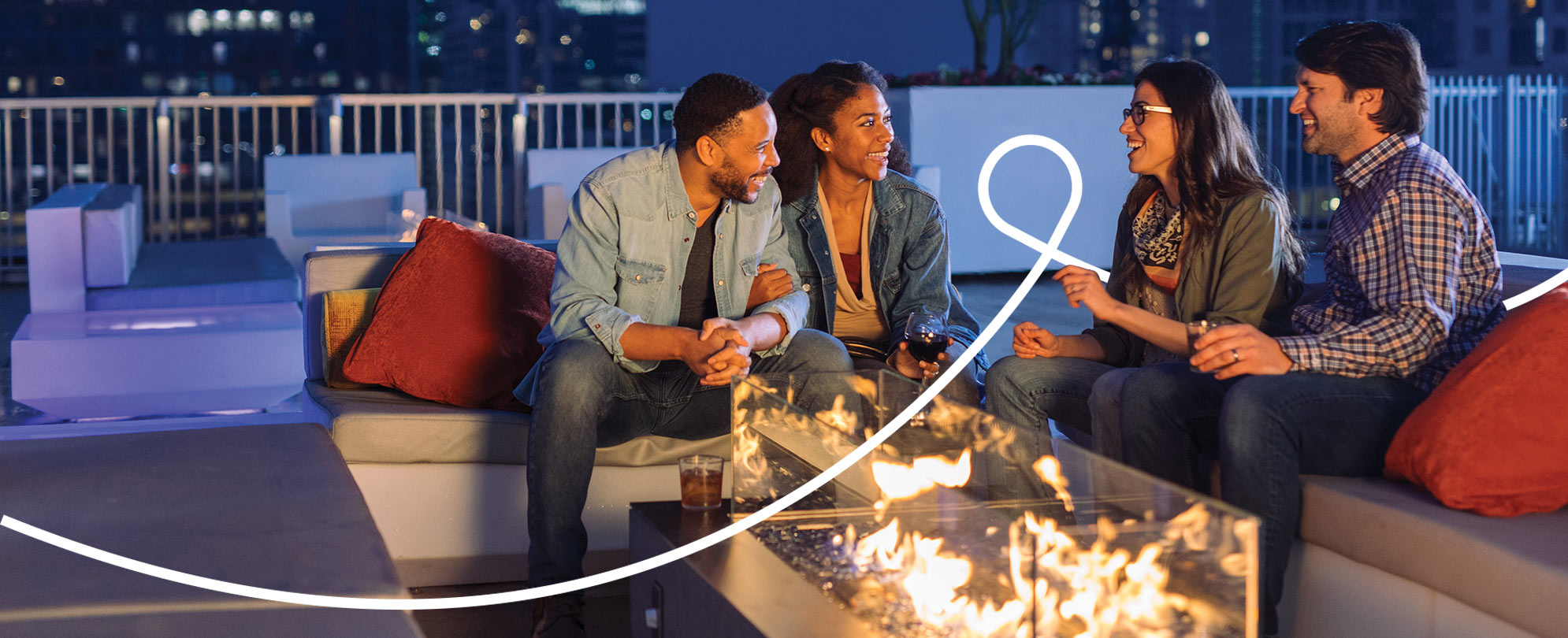 Two couples sitting and talking around a glass fire pit at the rooftop deck of a WorldMark resort.