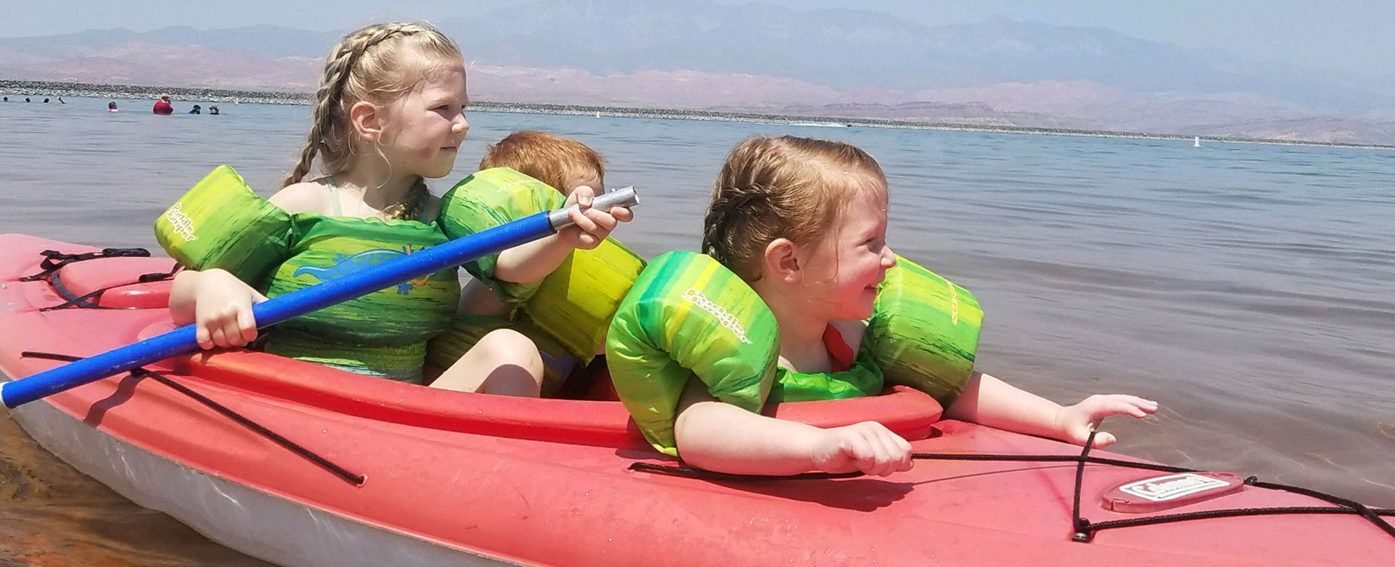 Three smiling kids in a kayak in the ocean.