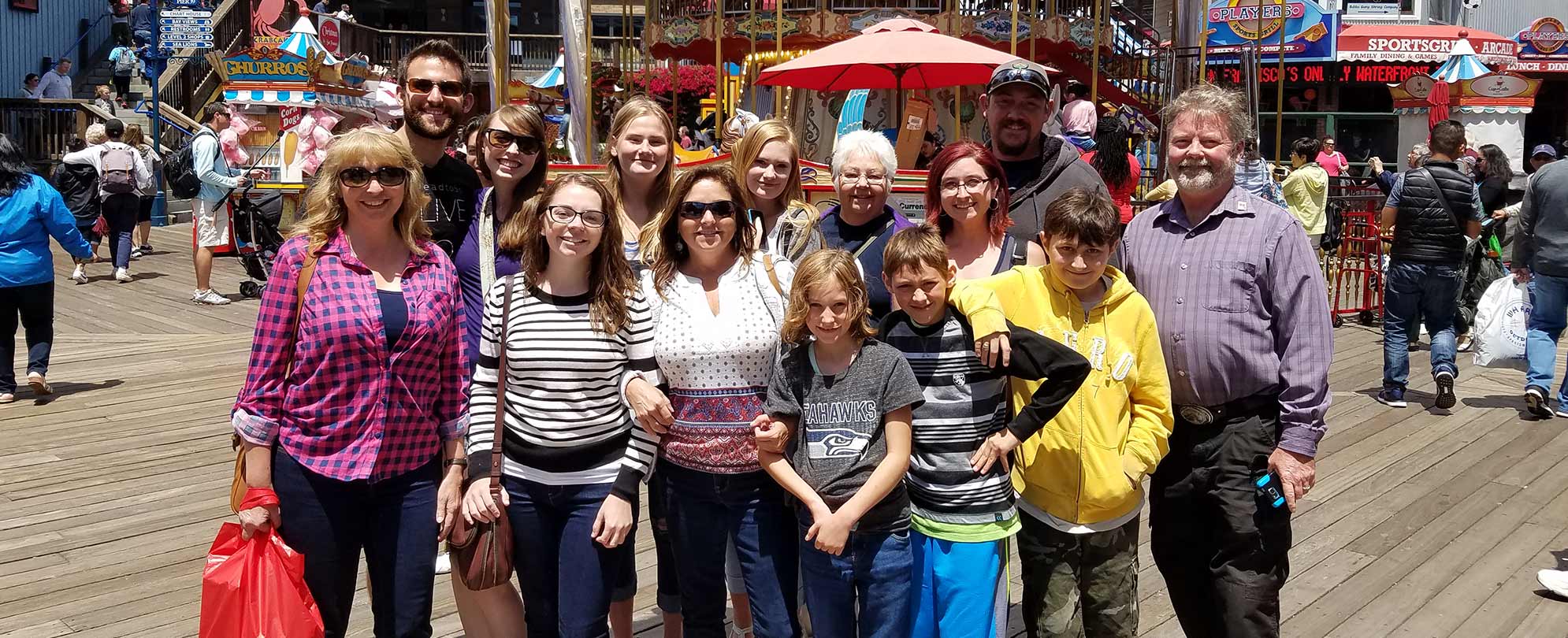 A family of 14 people poses for a picture on a busy boardwalk.