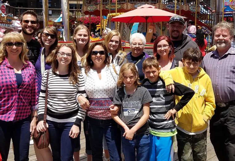 A family of 14 people poses for a picture on a busy boardwalk.