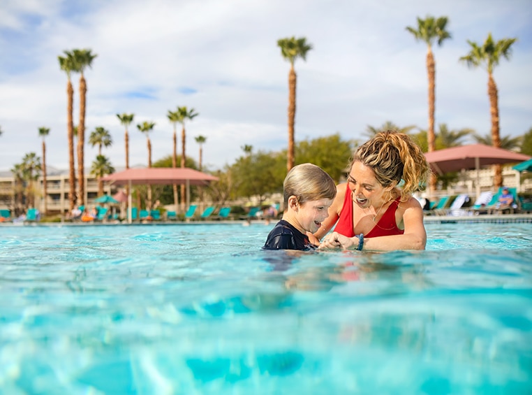 Mom in a red swimsuit and her son smile and splash in a pool on their WorldMark by Wyndham timeshare vacation.